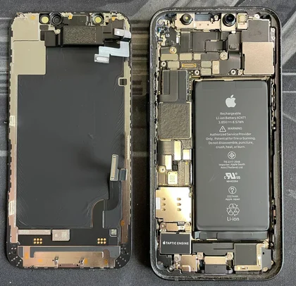 Photo d’un iPhone ouvert : écran d’un côté, châssis et batterie de l’autre, logos Apple visibles sur les pièces