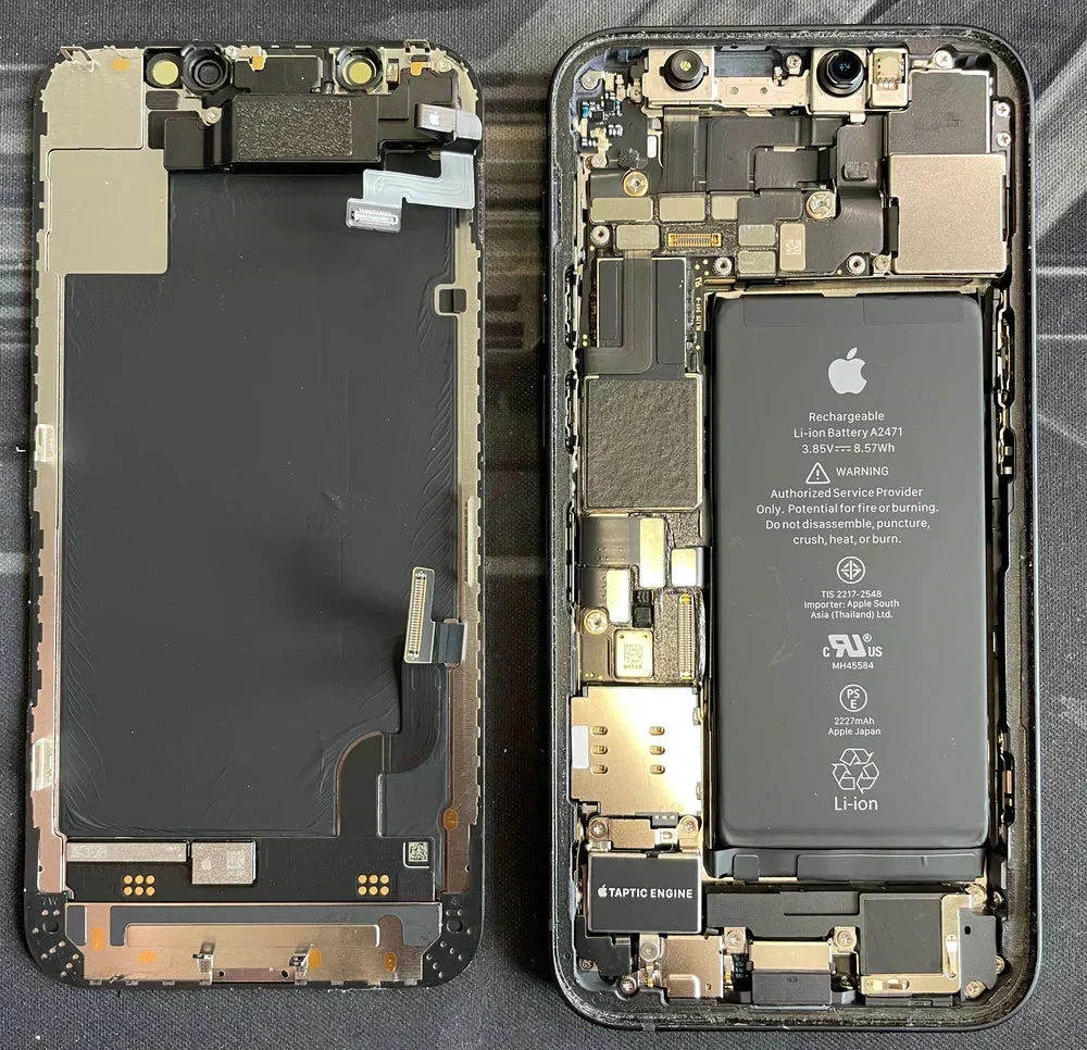 iPhone ouvert en deux dans notre atelier : écran d’un côté, châssis et batterie de l’autre. Les logos Apple sont visibles sur la nappe de l’écran, la batterie, la dalle et le Taptic Engine.